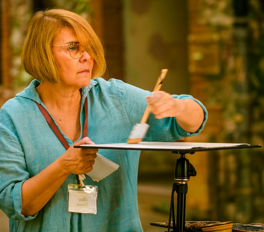 Manu in a blue shirt holding a paintbrush and a palette, with a blurred background